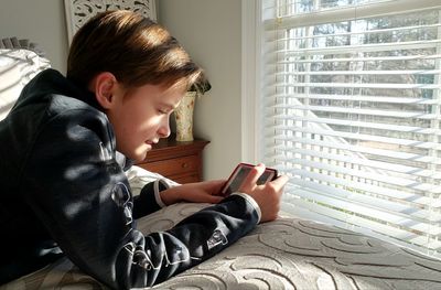 Young boy laying on bed using mobile device.