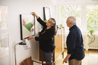 Senior man looking at woman hanging picture frame at home