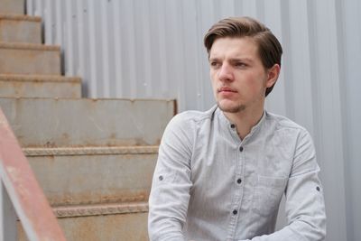 Thoughtful young man looking away while sitting on steps