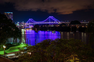 Illuminated bridge over river in city at night