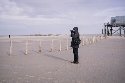 Rear view of man standing on beach against sky