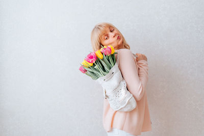  mature woman holding a backpack with bouquet tulip. flowers delivery. white background, copy space