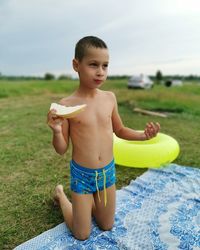 A seven-year-old child in swimming trunks eats a melon in nature