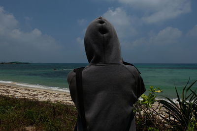 Rear view of man standing at beach against sky