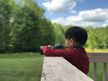 Rear view of girl holding camera against trees