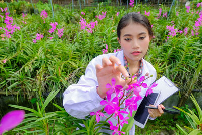 Portrait of woman holding pink flower on field