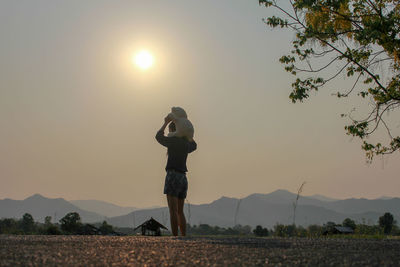 Woman with teddy bear standing on land against sky during sunset