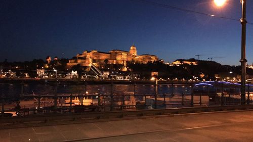 Illuminated city by river against clear sky at night