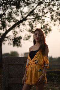 Portrait of young woman standing against tree