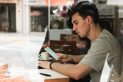 Male freelancer using laptop and smartphone in cafeteria