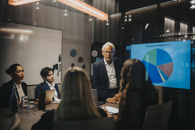 Senior businessman discussing ideas with male and female colleagues in board room