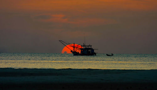 Silhouette fishing boat in sea against sky during sunset