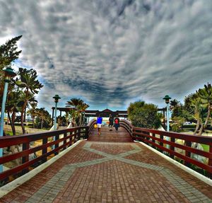 People walking on road against cloudy sky