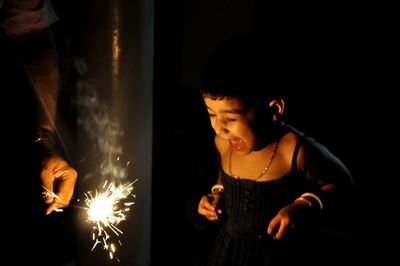 Cheerful girl standing by person holding sparkler at night