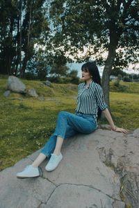 Woman sitting on rock against trees
