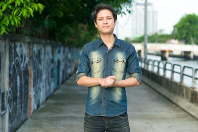 Portrait of young man standing against railing