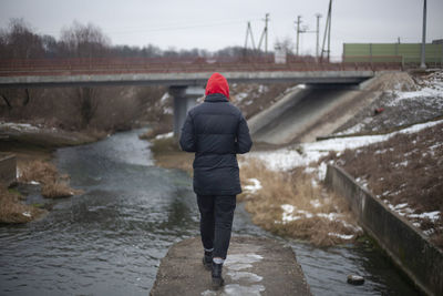 Rear view of woman standing in canal during winter