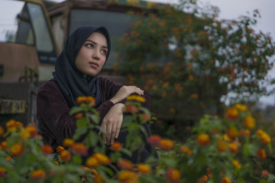 Thoughtful young woman sitting by flowers