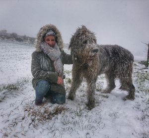 Woman with dog crouching on snow covered land against sky