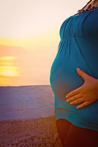 Midsection of woman standing on beach against sky during sunset