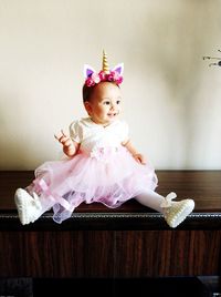 Full length of cute smiling baby girl sitting on cabinet at home