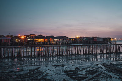 Illuminated buildings by sea against sky at sunset