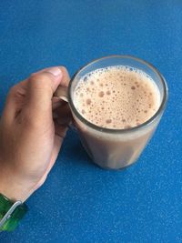 Cropped image of hand holding coffee cup against blue background