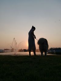 Man standing on shore against sky during sunset