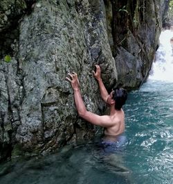 Shirtless man touching rock in sea