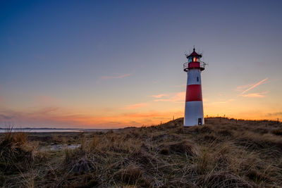 Lighthouse by building against sky during sunset