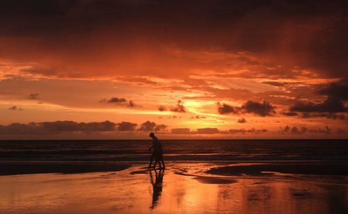 Silhouette man on beach against sky during sunset
