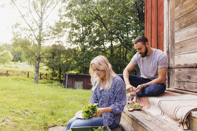 Friends cutting organic vegetables together while sitting outside cottage