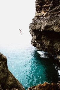 Man jumping from cliff into sea