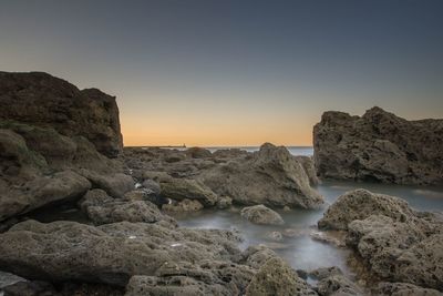 Rocks by sea against clear sky during sunset