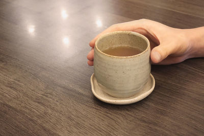 Close-up of hand holding coffee cup on table