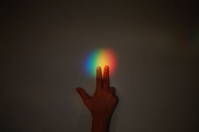 Cropped image of hand touching multi colored sunlight on wall