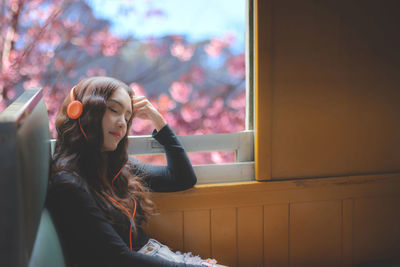 Young woman looking away while sitting on window