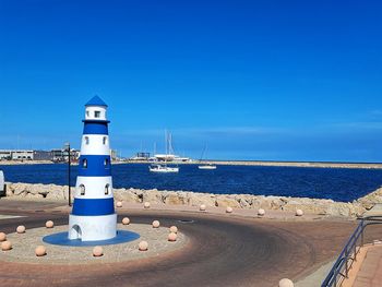 Lighthouse by sea against clear blue sky