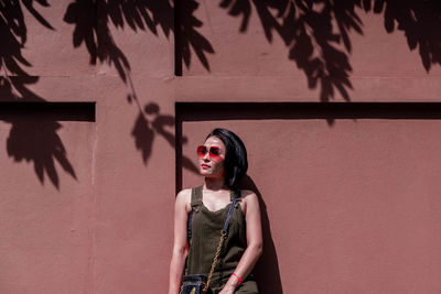 Woman looking away while standing against wall outdoors