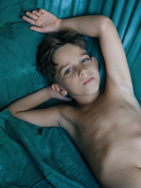 High angle portrait of shirtless boy lying on bed