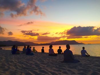Silhouette people doing yoga on sandy beach during sunset