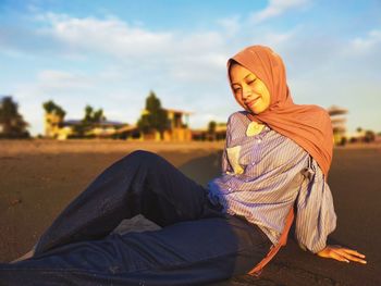 Midsection of young woman sitting on land against sky