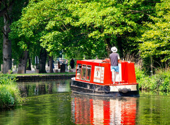Red boat in lake against trees in city