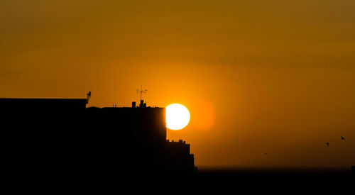 Low angle view of silhouette building against orange sky