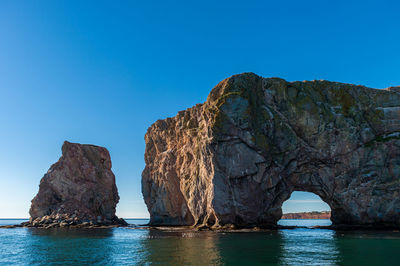 Rock formation in sea against clear blue sky