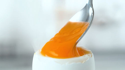 Boiled eggs in egg cups with a hand scooping some egg out of one with a small spoon.