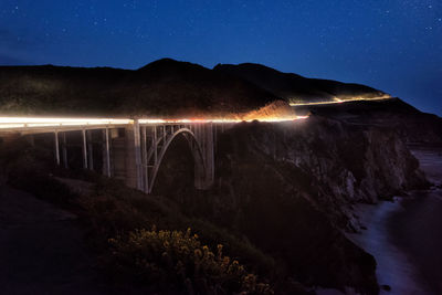 Illuminated arch bridge over river against sky at night