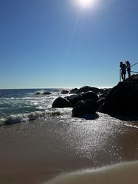 People on beach against clear sky during sunny day