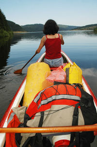 Rear view of man sitting on lake against sky