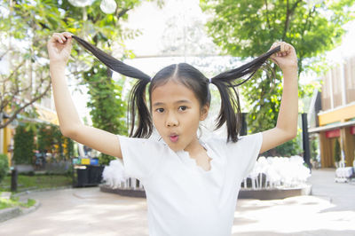 Portrait of cute girl holding pigtails while standing at park